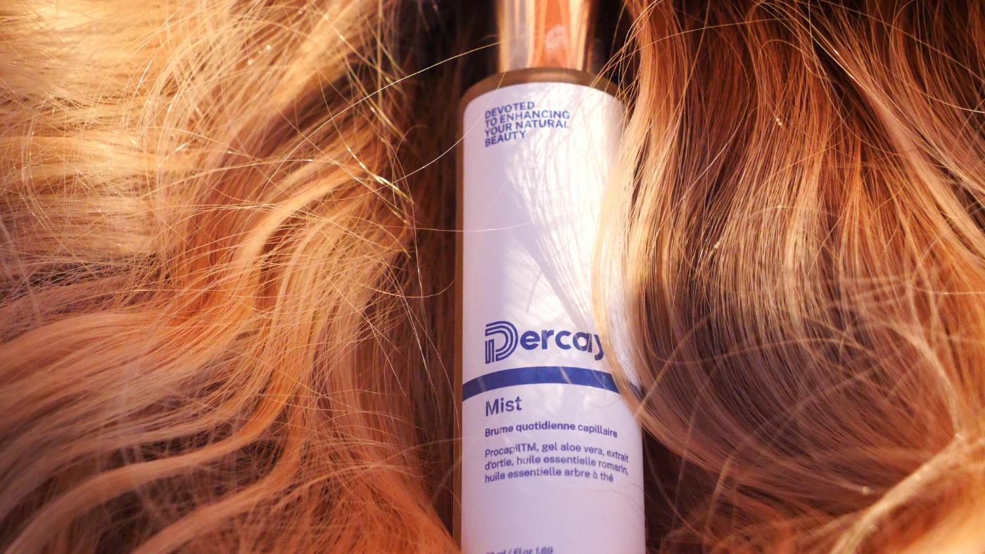 L'image montre un flacon de produit capillaire de marque "Dercay" posé sur des cheveux roux ondulés.