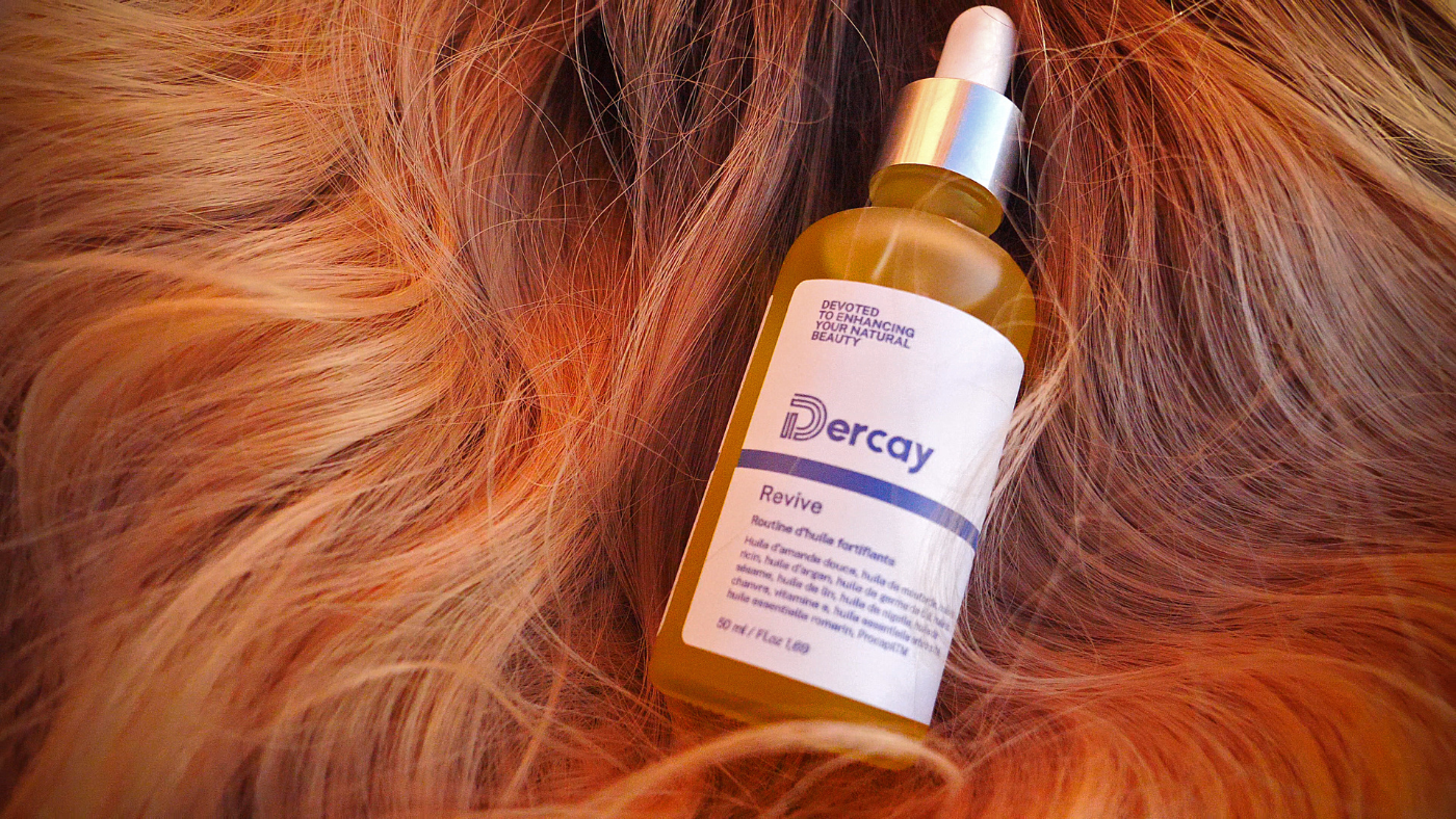 L'image montre un flacon de produit capillaire de marque "Dercay" posé sur des cheveux roux ondulés.
