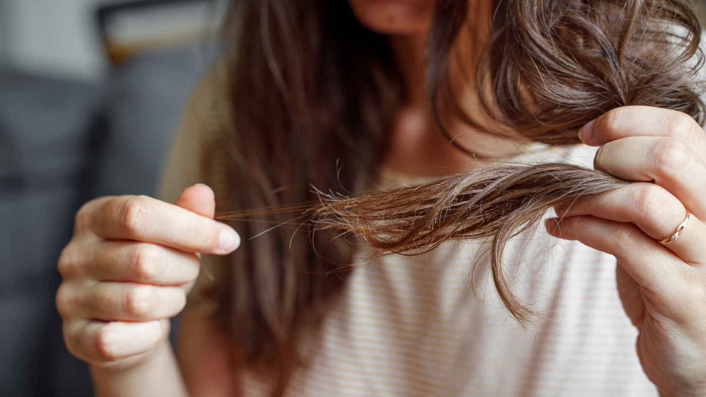 Femme inquiète examinant ses cheveux dans le miroir, signe de perte de cheveux.