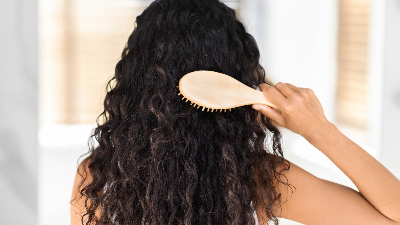 Femme se brossant les cheveux bouclés avec une brosse en bois.