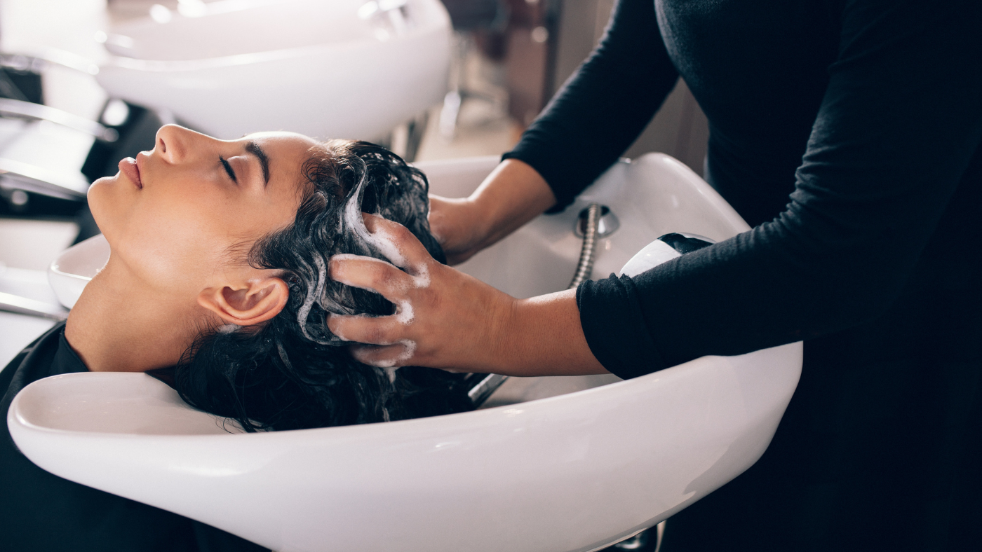 Une femme dans un salon de coiffure se faisant laver les cheveux avec shampooing par une coiffeuse.