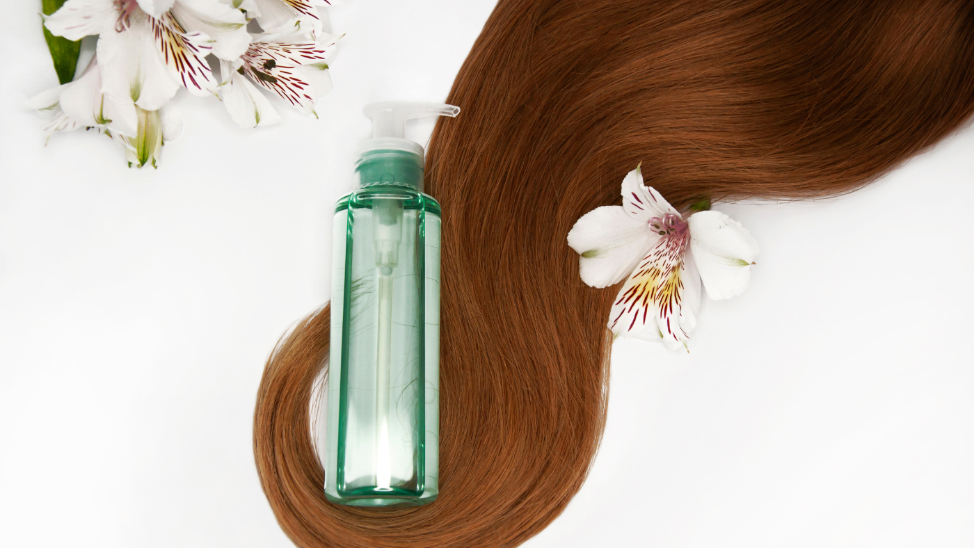 Un flacon de shampoing en verre avec une étiquette rose et un bouchon blanc se trouve à côté d'un bouquet de fleurs roses et blanches sur un fond blanc.